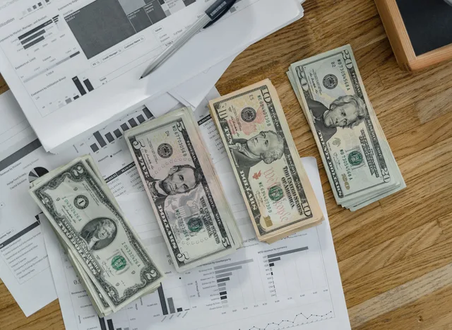 Stacks of US Dollar banknotes placed over financial documents and reports on a desk. Building a monthly inbound demand review