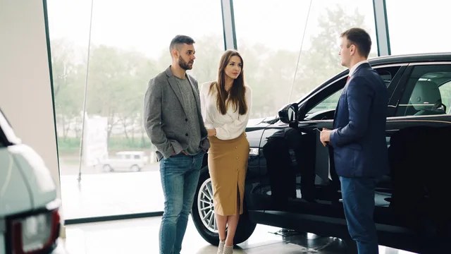 A couple converses with a salesperson about buying a car inside a dealership. Choosing buying questions that can lead to a relevant enquiry