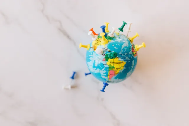 A globe decorated with colorful push pins on a marble surface represents global connections. Handling enquiries outside the service area