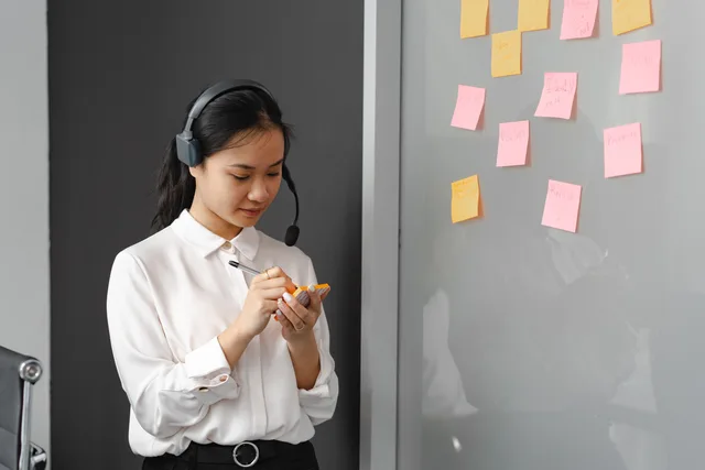 A woman in a call center writing on sticky notes with a headset indoors. Lead volume versus accepted sales enquiries