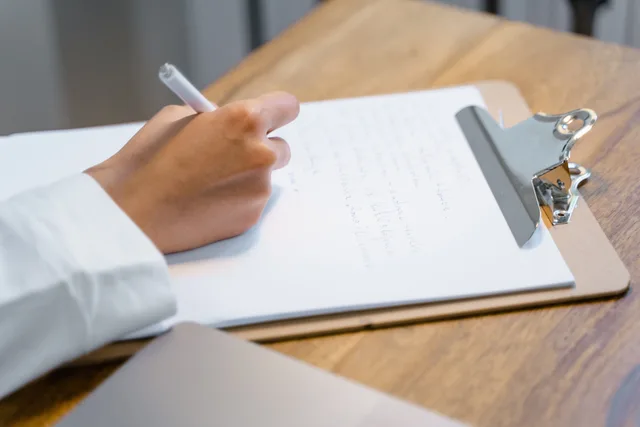 A close-up of a person's hand writing on a clipboard on a wooden table, displaying focus and concentration. Selecting form fields that help qualification